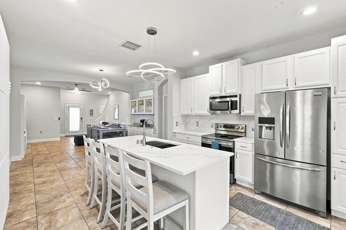 A modern kitchen with white cabinetry, stainless steel appliances, and a central island with bar stools.