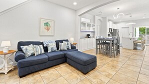 A modern living room with a sectional sofa, a dining table with chairs, and a kitchen area with white cabinets. - 3 Bedroom House with Hot Tub Close to Downtown and Stadiums (Tampa)