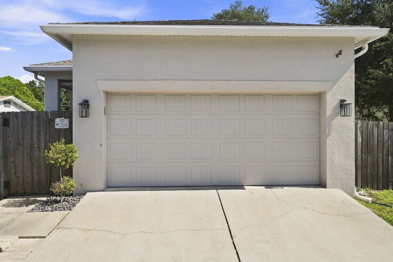 A garage with a white door, a concrete driveway, and a wooden fence.