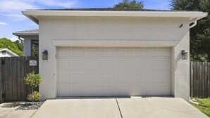 A garage with a white door, a concrete driveway, and a wooden fence. - 3 Bedroom House with Hot Tub Close to Downtown and Stadiums (Tampa)