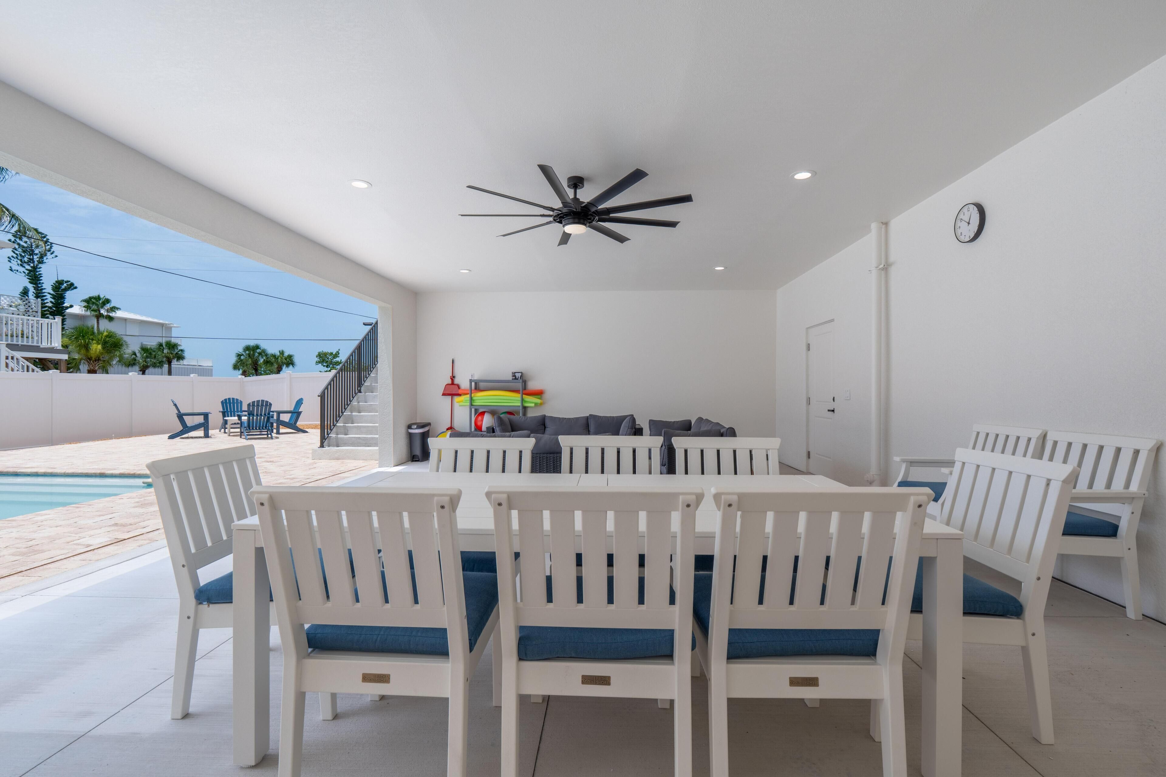 An outdoor patio with a pool, white furniture, and a ceiling fan.