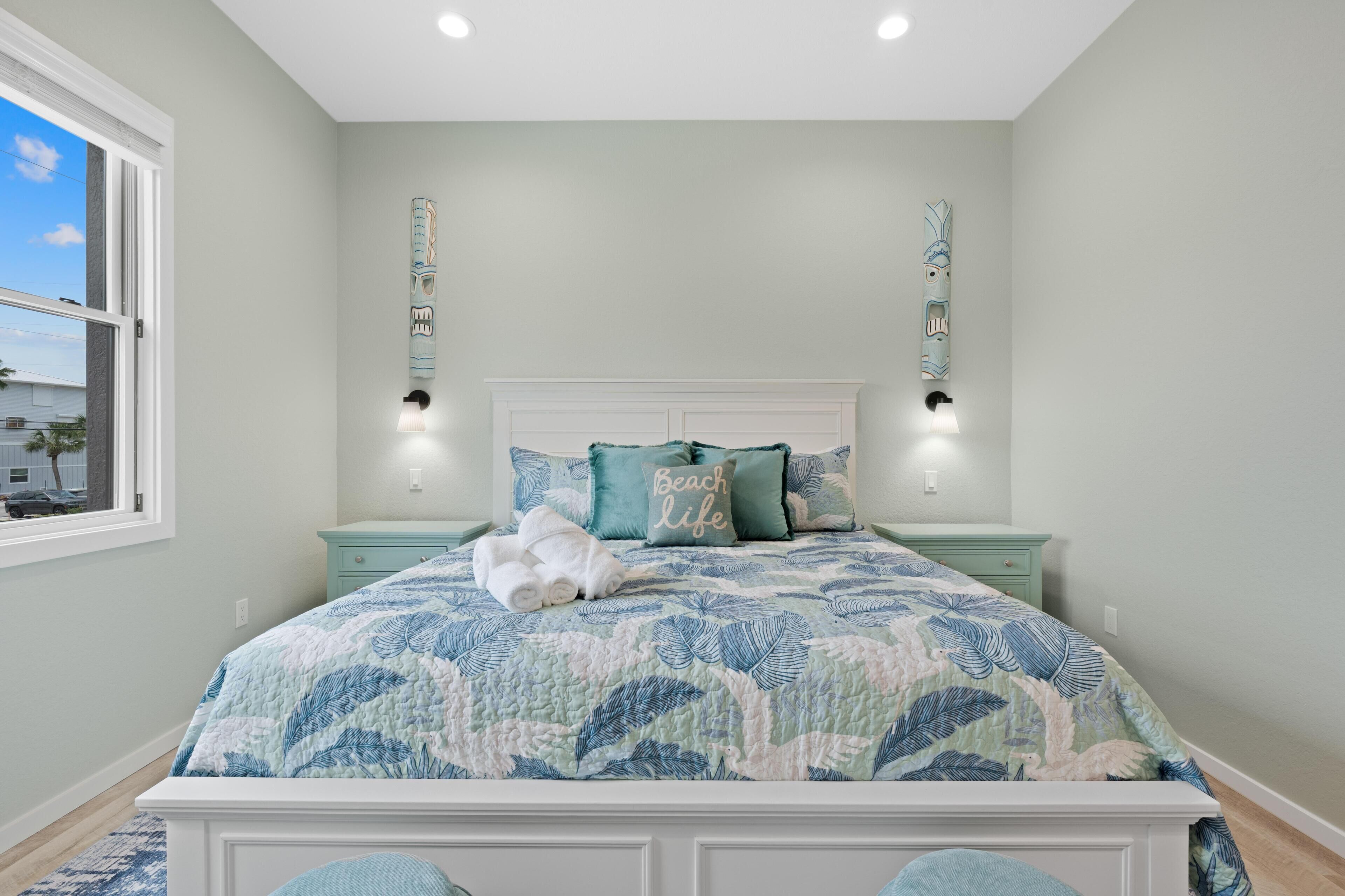 A bedroom with a bed, nightstands, a window, and a view of the outside.