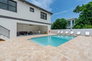 A modern outdoor pool area with a covered seating area and a white fence. - Seaside Cottage (Fort Myers Beach)