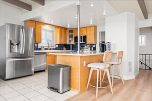 A modern kitchen with stainless steel appliances, wooden cabinets, and a central island with bar stools. - Waterfront Retreat w/ Dock, Hot Tub & Views (Bethel Island)