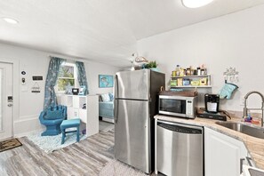 Una cocina compacta con refrigerador, microondas, cafetera y un lavamanos.