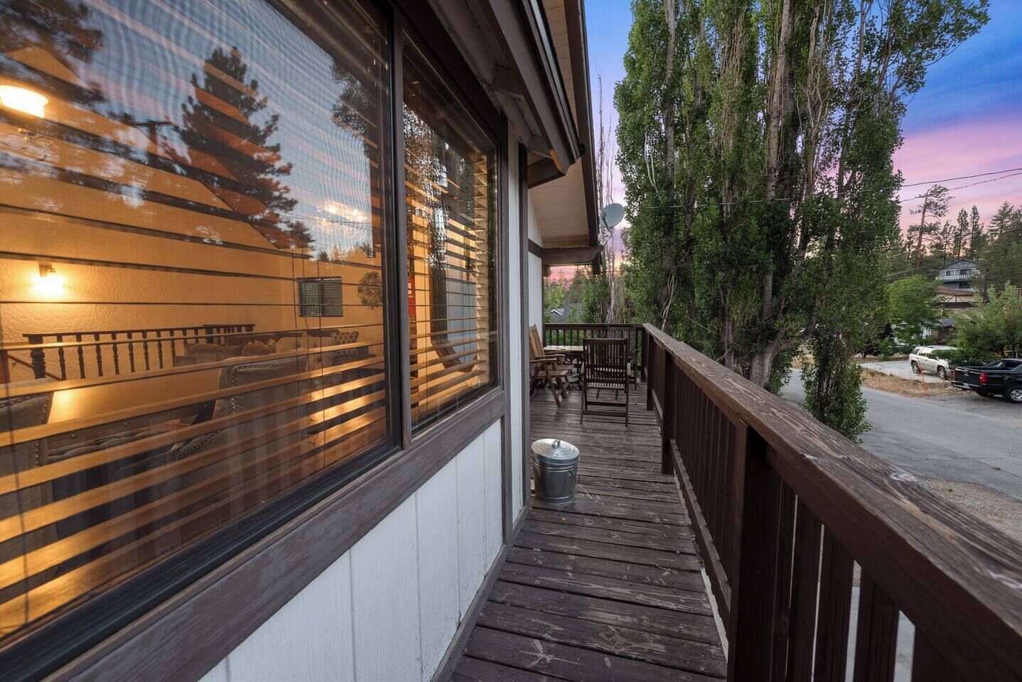A wooden deck with outdoor furniture, a trash can, and a view of a street with parked cars and trees.