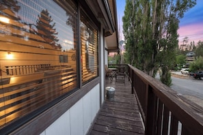 A wooden deck with outdoor furniture, a trash can, and a view of a street with parked cars and trees. - Private Cabin | Sleeps 8 | Game Room | BBQ (Big Bear Lake)