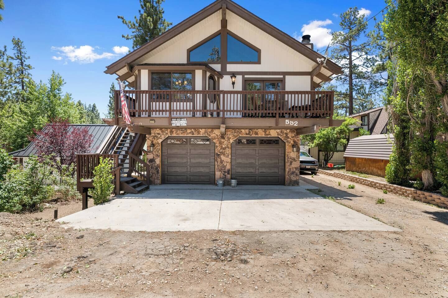 A two-story house with a balcony, two garage doors, and a stone facade.