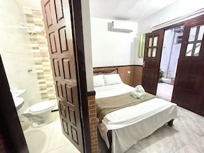 Een hotelkamer met een bed, een toilet en een airconditioning aan de muur.