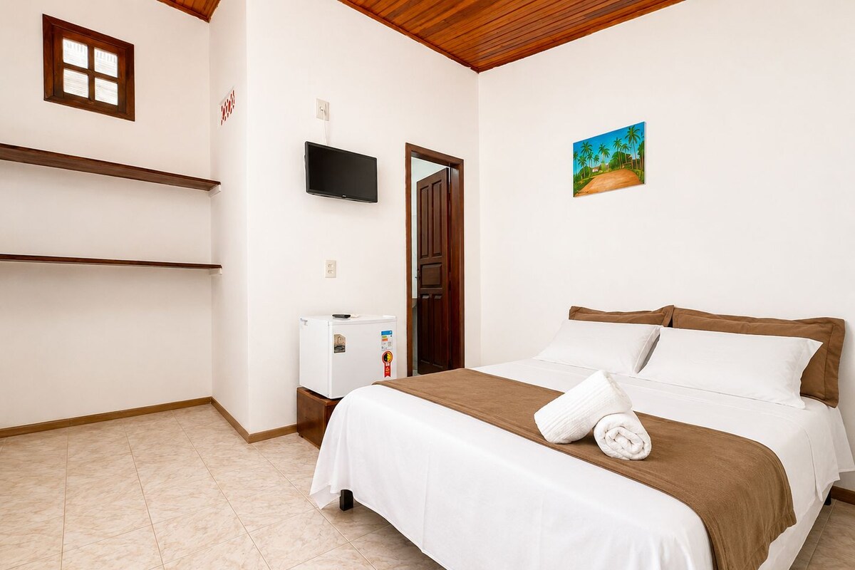 Habitación de hotel con cama, televisor, refrigerador pequeño y un cuadro en la pared.