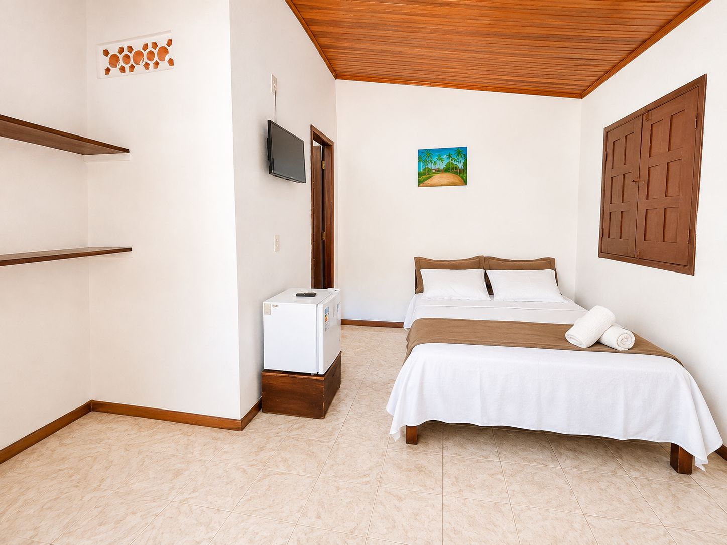 Quarto com cama, televisão, frigorífico e porta de madeira.