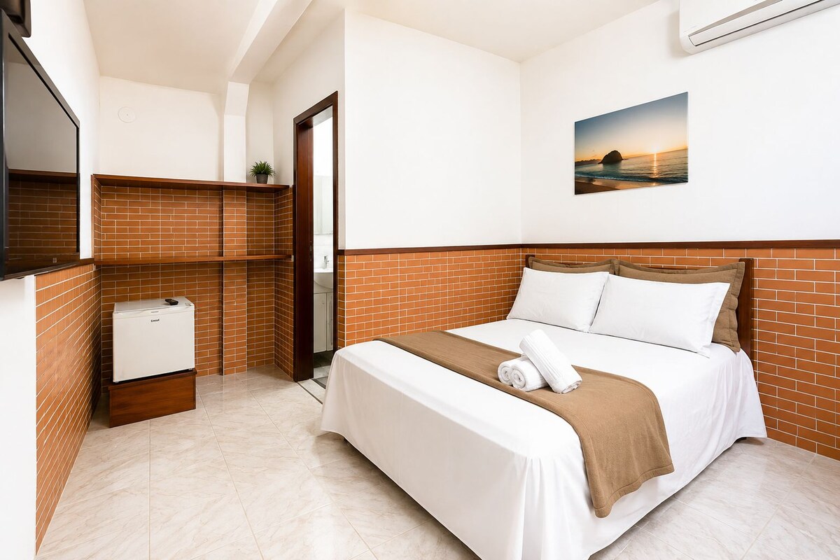 Habitación de hotel con cama, un refrigerador pequeño, un espejo y una imagen de un atardecer.
