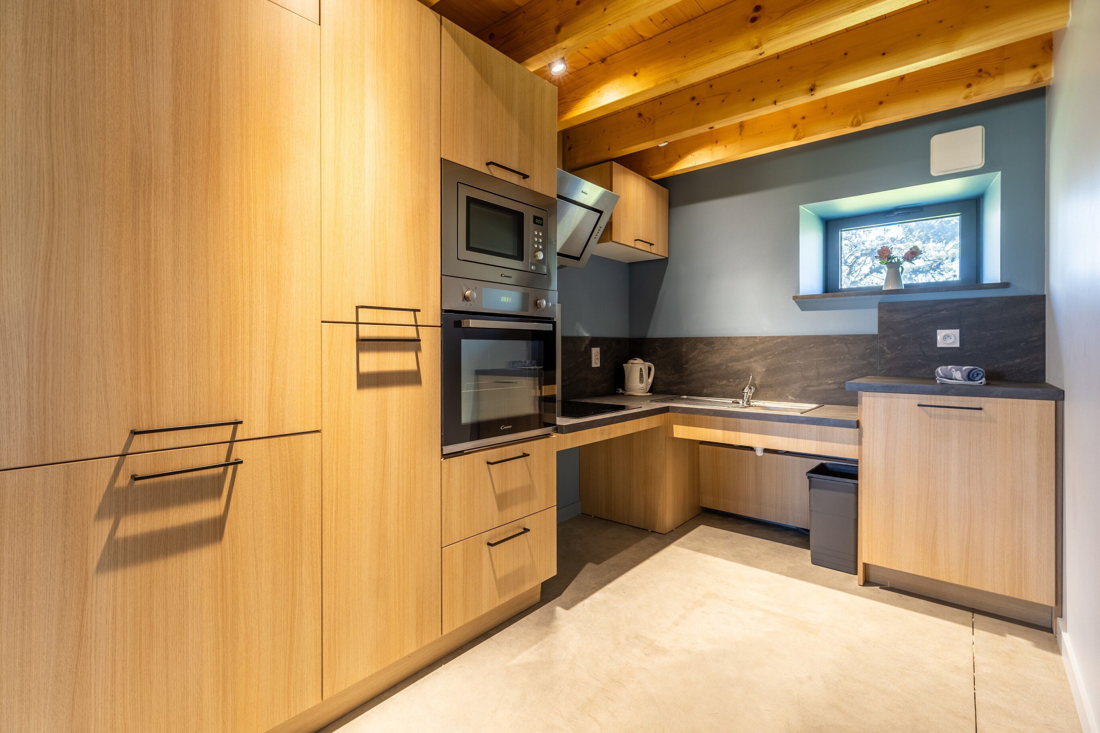Una cocina moderna con gabinetes de madera, microondas integrado, horno y una ventana sobre el fregadero.