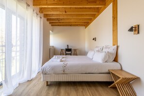 A bedroom with a wooden ceiling, a bed with white bedding, a small table, and a chair.