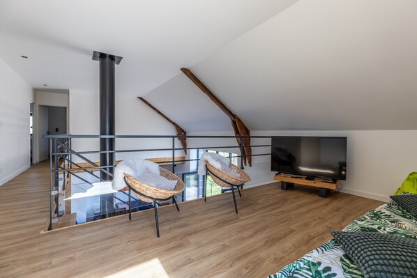 A modern living room with a glass balustrade, a large TV, and two wicker chairs.