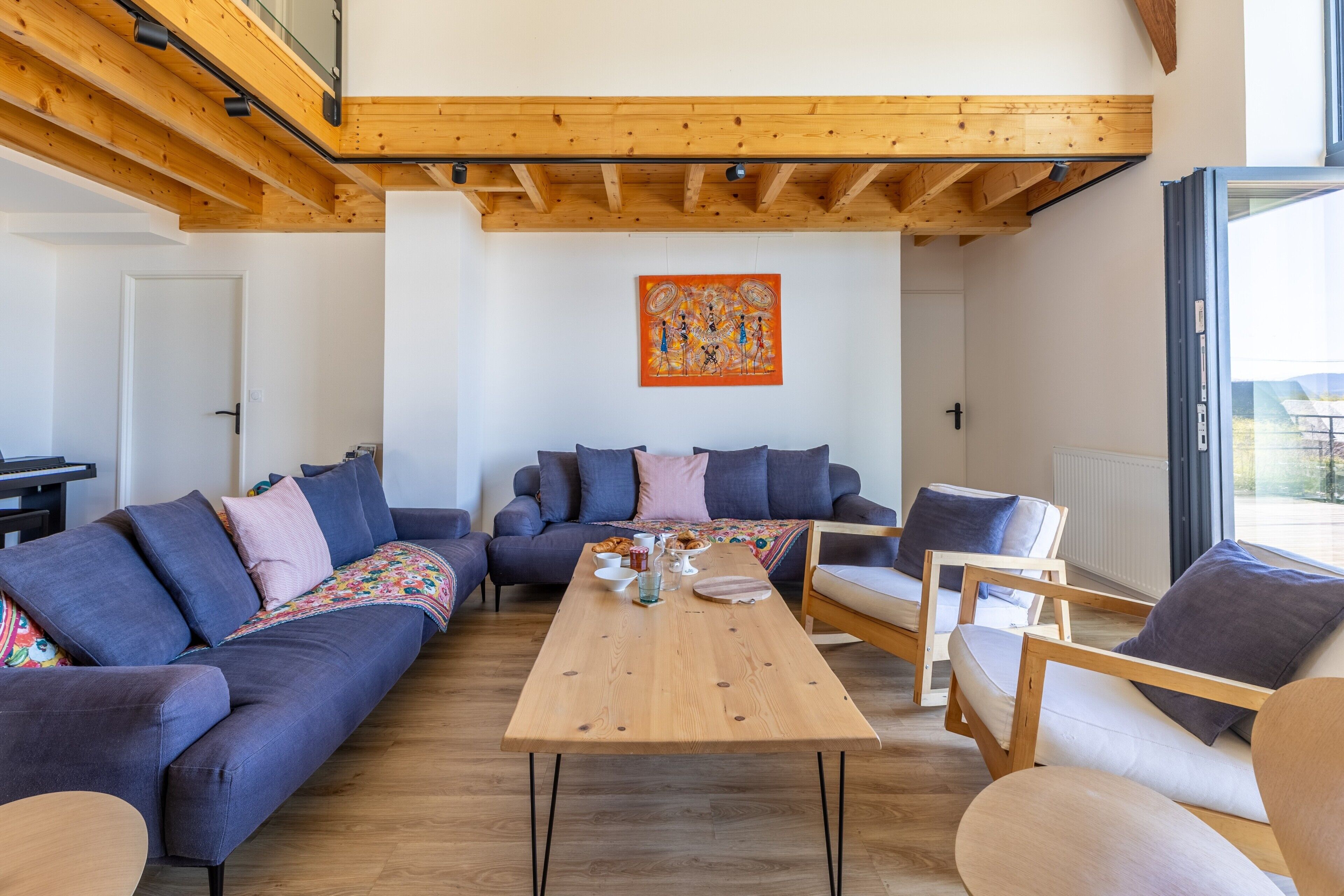 Una sala de estar moderna con techo de madera, un amplio sofá, una mesa de centro y un cuadro en la pared.
