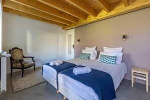 A bedroom with two beds, a chair, a small table, and a door.
