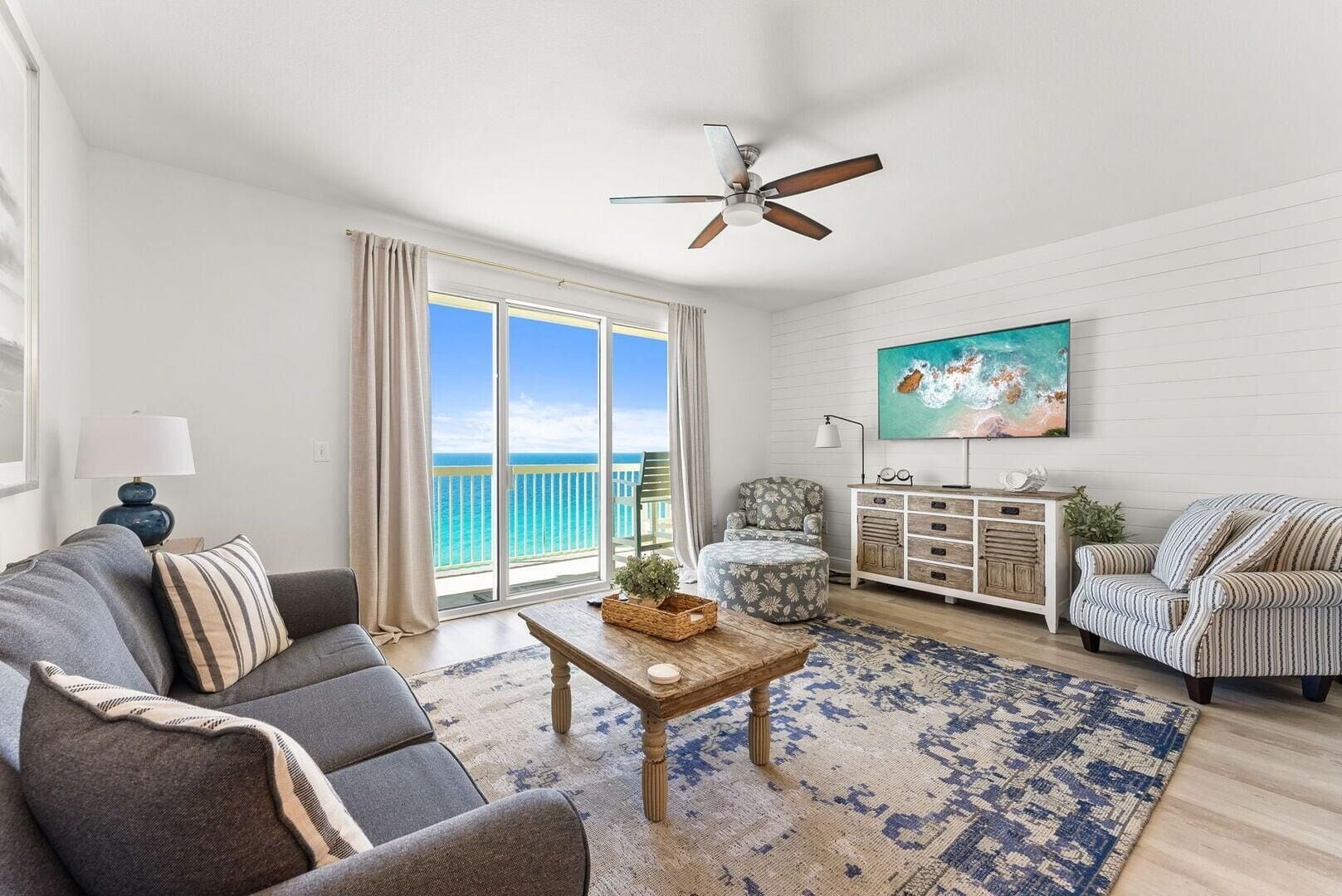 A spacious living room with a large window, a ceiling fan, a sofa, a coffee table, and a television.