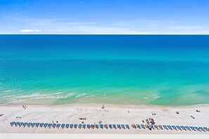A beach with rows of sun loungers and umbrellas, a clear blue sky, and the ocean. - Celadon 1503 (Panama City Beach)
