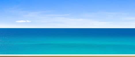A clear view of a turquoise ocean from a balcony with a wooden railing.