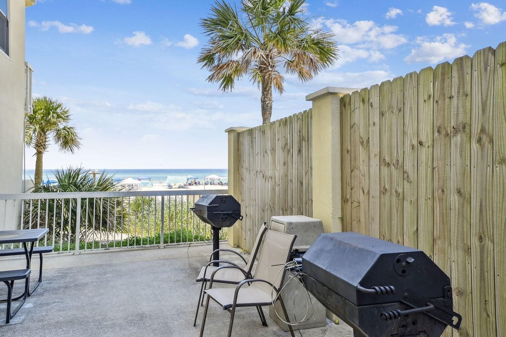 Un balcon avec vue sur la plage, une clôture en bois, un barbecue et des meubles pour se détendre à l’extérieur.