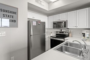 Eine Küche mit einem Edelstahlkühlschrank, einer Mikrowelle, einem Backofen und einem Spülbecken.