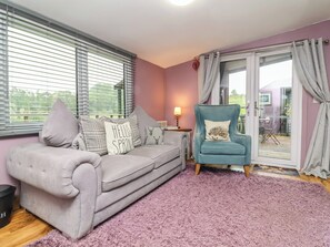 A living room with a grey sofa, a teal armchair, and a purple shag rug. - Hedgehogs Lodge (South Molton)