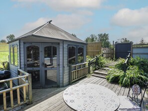 A gazebo with a wooden deck, a round table, and a barbecue grill. - Hedgehogs Lodge (South Molton)