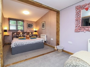A bedroom with a bed, two bedside lamps, a radiator, a window with blinds, and a mirror on the wall. - Hedgehogs Lodge (South Molton)