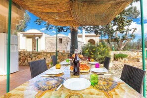 Zona pranzo all'aperto con tavolo per due, una bottiglia di vino e una pizza.