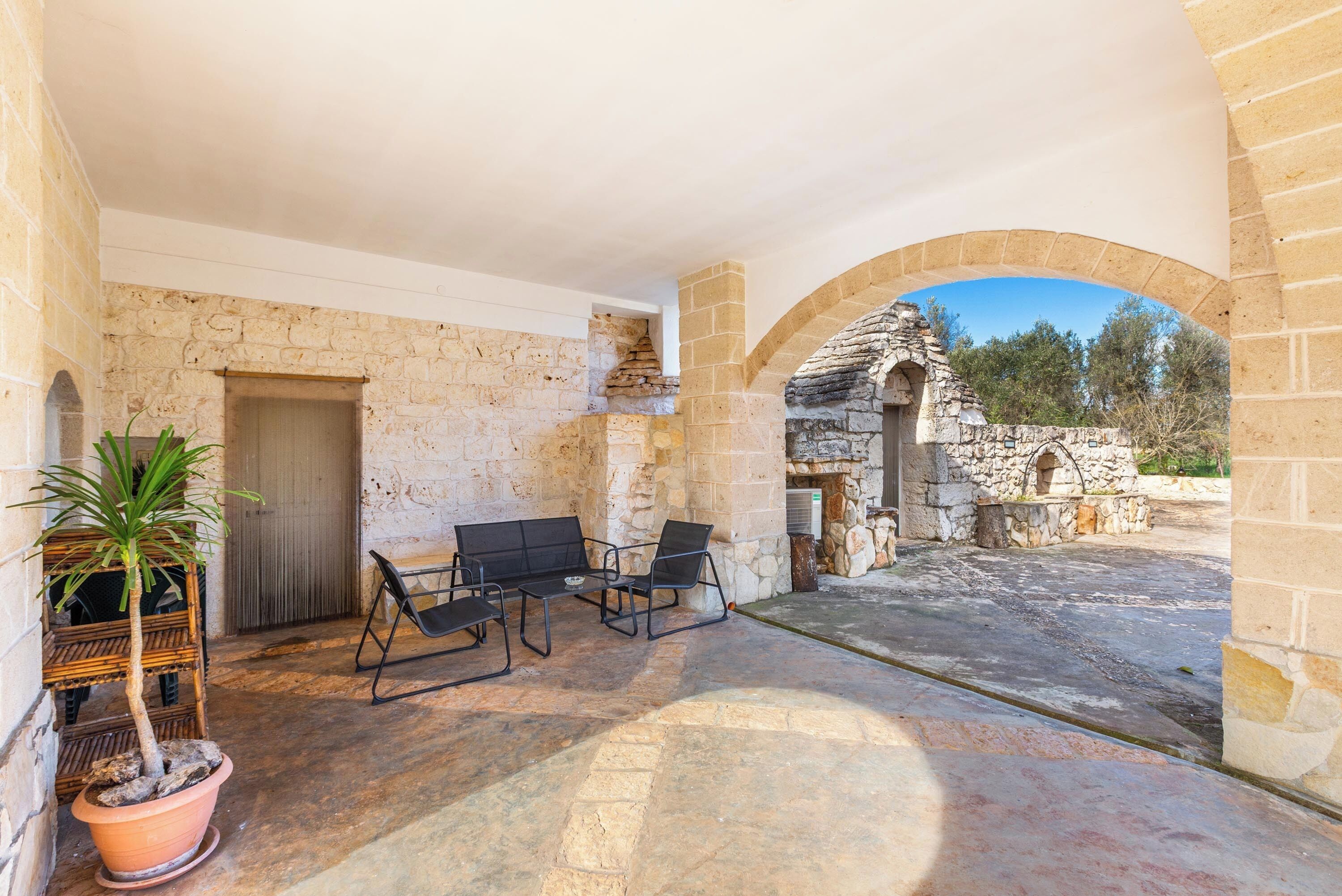 A courtyard with stone walls, a wooden door, a bench, and a potted plant.