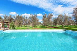Una piscina trasparente circondata da alberi e da un'area verde.
