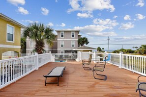 A wooden deck with a pool, chairs, and a view of a building and ocean. - Happy Times @ Laguna (Panama City Beach)