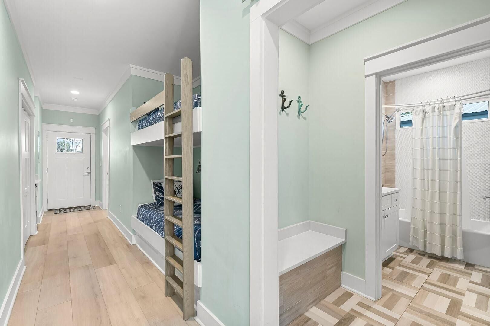 Un couloir avec un lit superposé, une porte et une salle de bain avec un rideau de douche.