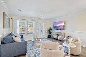 A living room with a sofa, armchair, coffee table, and a TV mounted on the wall. - It's a Shore Bet (Panama City Beach)