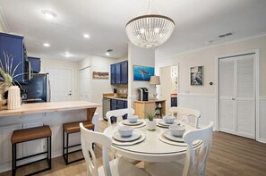 A modern kitchen with a central island, white cabinetry, and a chandelier. - It's a Shore Bet (Panama City Beach)