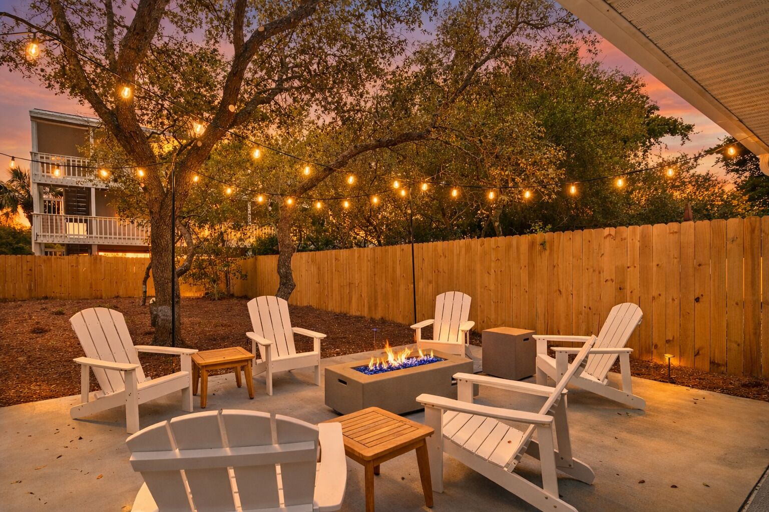 Une terrasse extérieure avec des fauteuils Adirondack, un foyer et des guirlandes lumineuses.