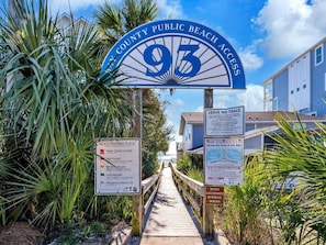 A beach access sign with a palm tree and a wooden walkway leading to beach houses. - It's a Shore Bet (Panama City Beach)