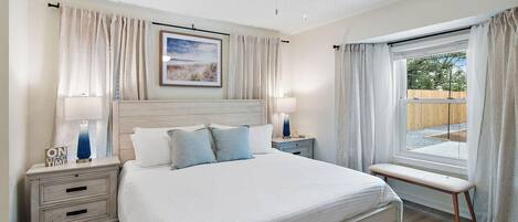 A bedroom with a bed, bedside tables, a ceiling fan, a window with curtains, and a framed picture on the wall.