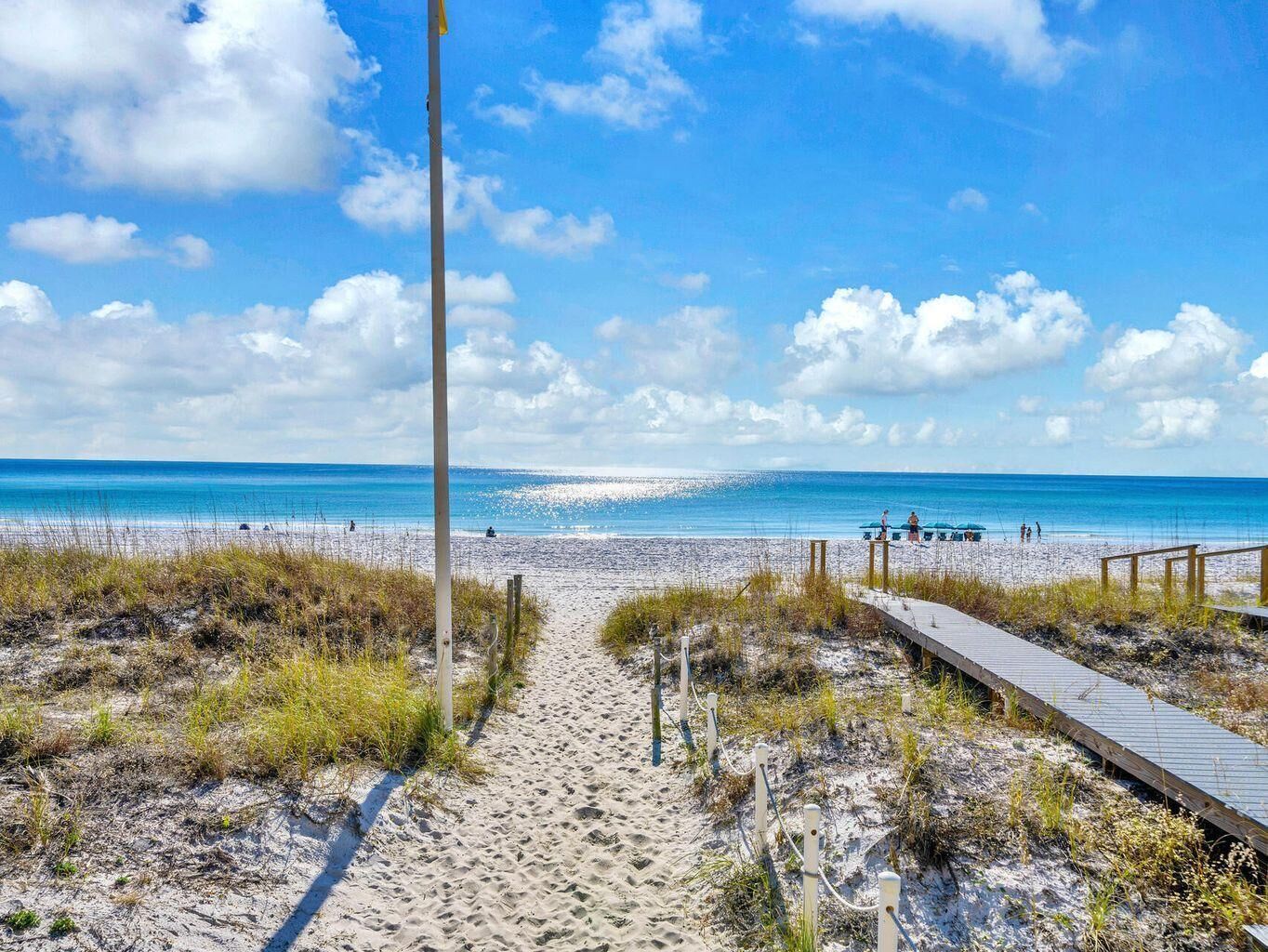 Ein sandiger Strand mit einem hölzernen Promenadenweg zum Wasser, bewölkter Himmel und ruhiges Meer.