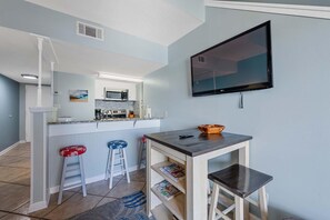 A kitchen with a microwave, a coffee maker, and a sink. There is a bar area with stools and a television mounted on the wall. - Sugar Beach 371 (Orange Beach)