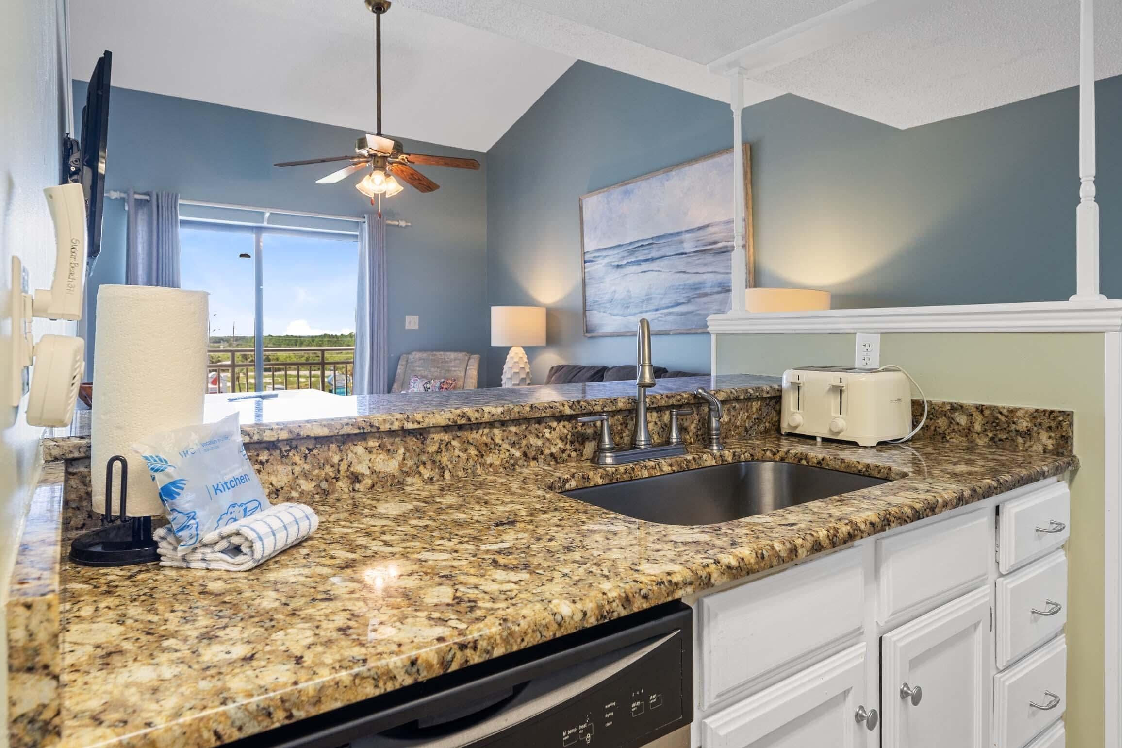 A kitchen with granite countertops, a dishwasher, a sink, and a ceiling fan.