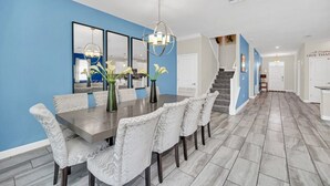 A dining area with a long table and chairs, a chandelier, and a blue accent wall. - 1583 Plunker 8BR / 5BA Champions Gate Villa near to Disney, Private Pool & Games (Four Corners)