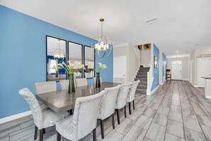 Uma sala de jantar com uma mesa comprida e cadeiras, um lustre e uma parede azul decorativa.