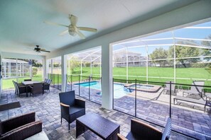 Um pátio externo com piscina, área de estar e vista para um gramado verde.