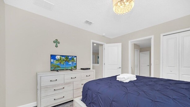 A bedroom with a bed, a dresser, a television, and a door. - 1583 Plunker 8BR / 5BA Champions Gate Villa near to Disney, Private Pool & Games (Four Corners)