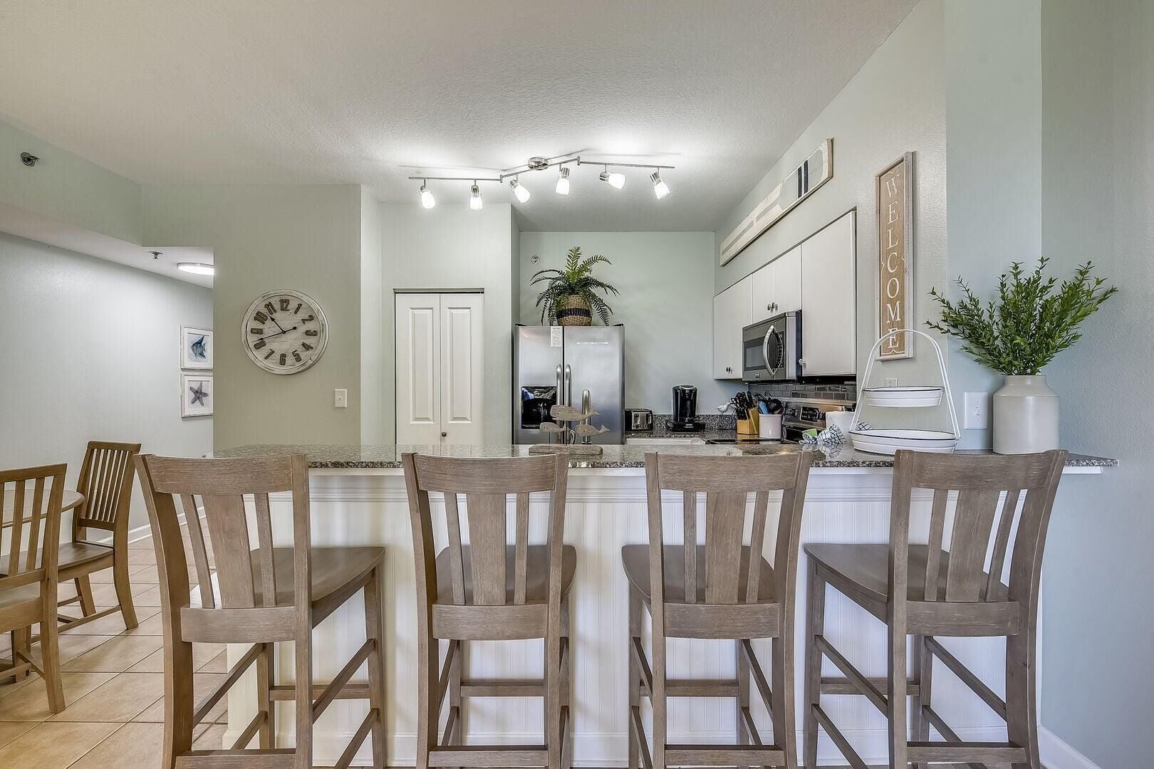 A modern kitchen with a central island, white cabinetry, and a dining area with wooden chairs.