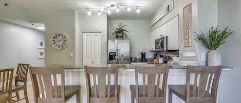 A modern kitchen with a central island, white cabinetry, and a dining area with wooden chairs.