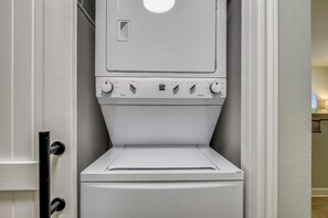 A front view of a white wall-mounted washer and dryer unit with control knobs and a door handle. - Shores of Panama 207 - Toes in the Sand (Panama City Beach)
