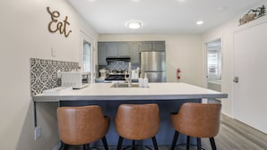 Una cocina moderna con una isla central, taburetes de bar y un elemento decorativo en la pared.